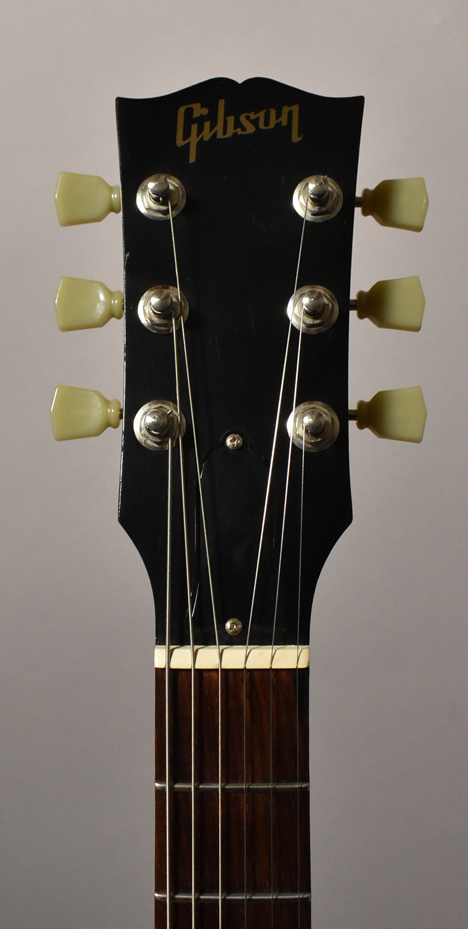 The black headstock, with six cream-colored tuning pegs, shows light wear and a small truss rod cover above the nut and dark fretboard.