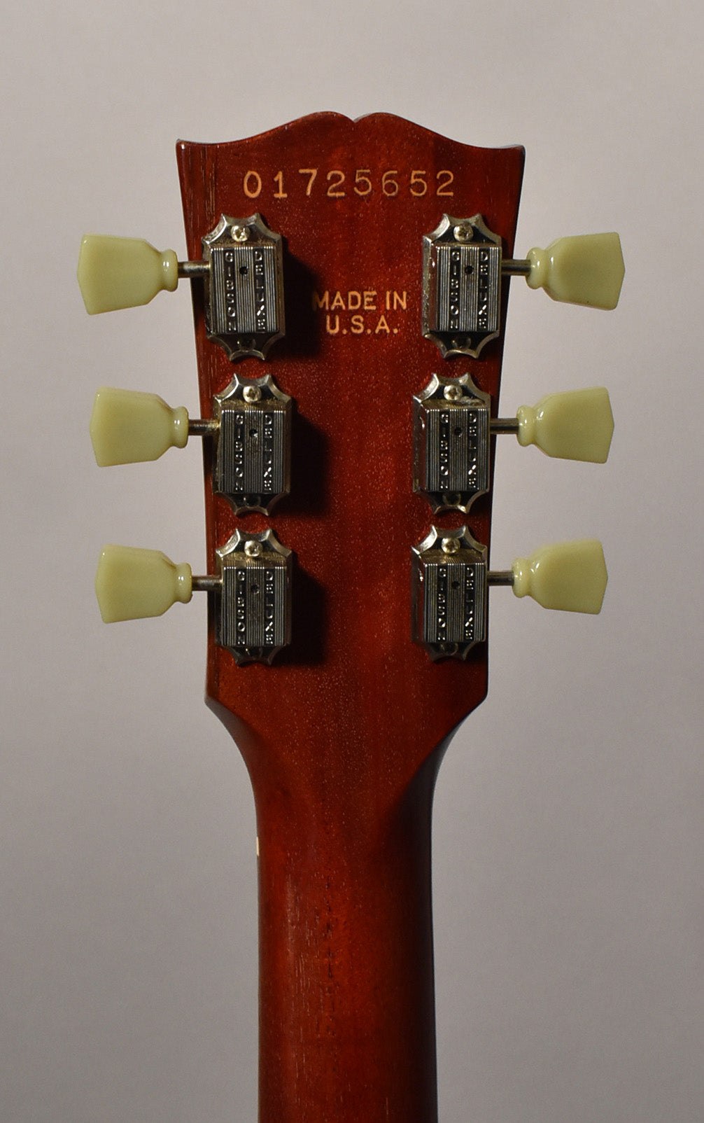 Rear view of the cherry-finished headstock and upper neck, showing six cream tuning pegs and chrome tuners with visible wear.