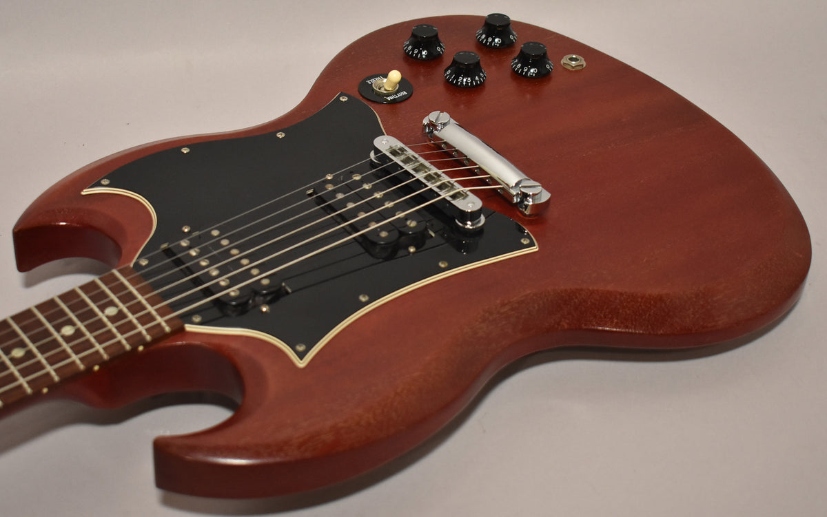 Angled view of a cherry red SG with a worn finish, black pickguard, two humbuckers, four black control knobs, and a chrome bridge.