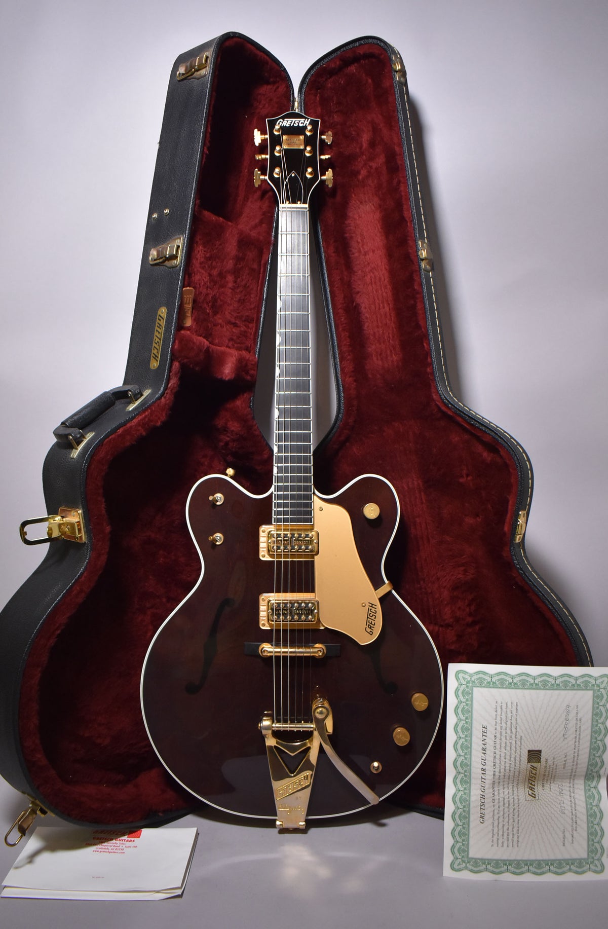 Full view of a dark walnut hollow-body electric guitar with gold hardware, white binding, and f-holes, standing in its open red-lined case.