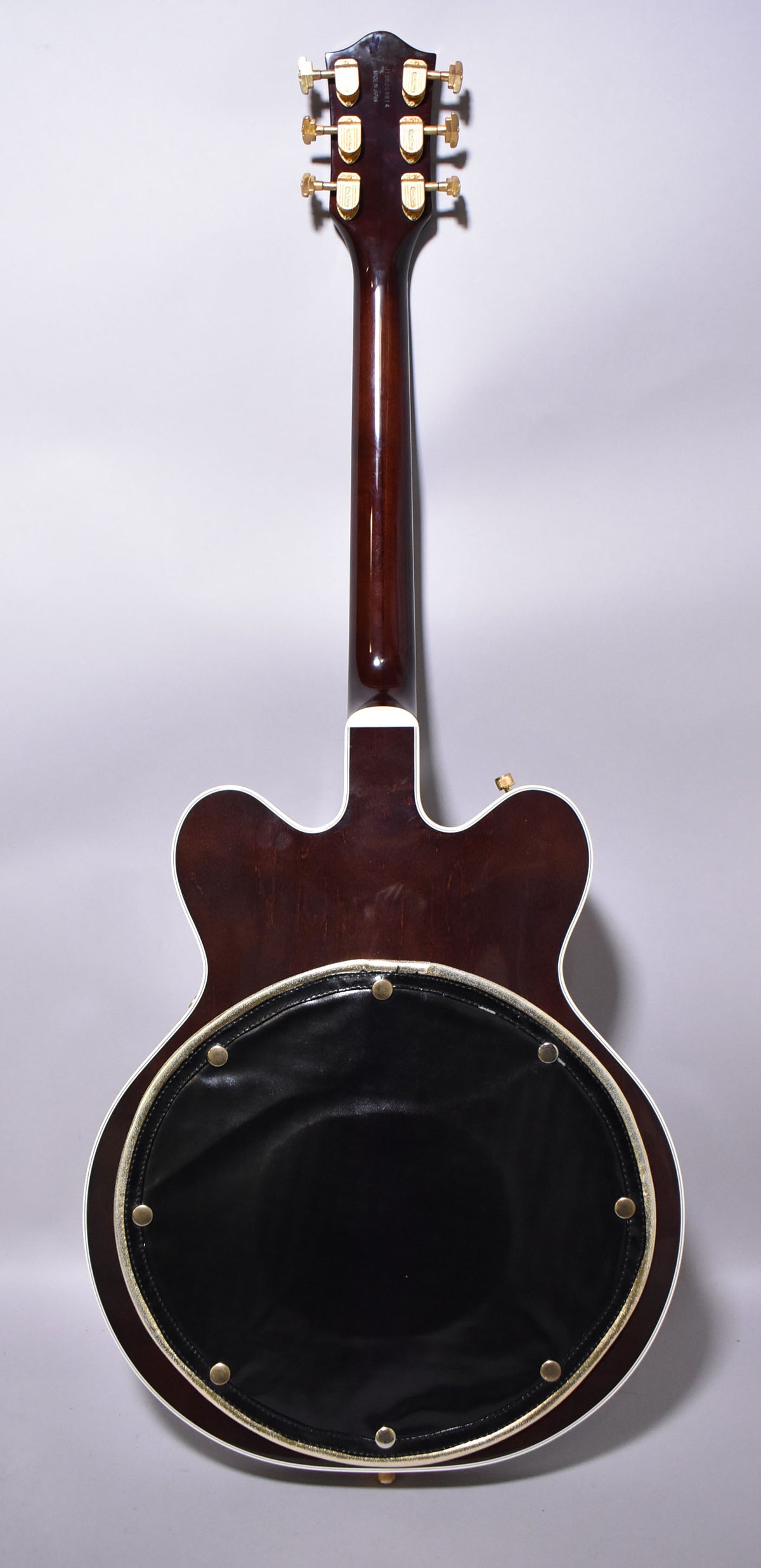 The guitar's back is dark walnut with white binding, featuring a large, round black leather pad with gold studs.
