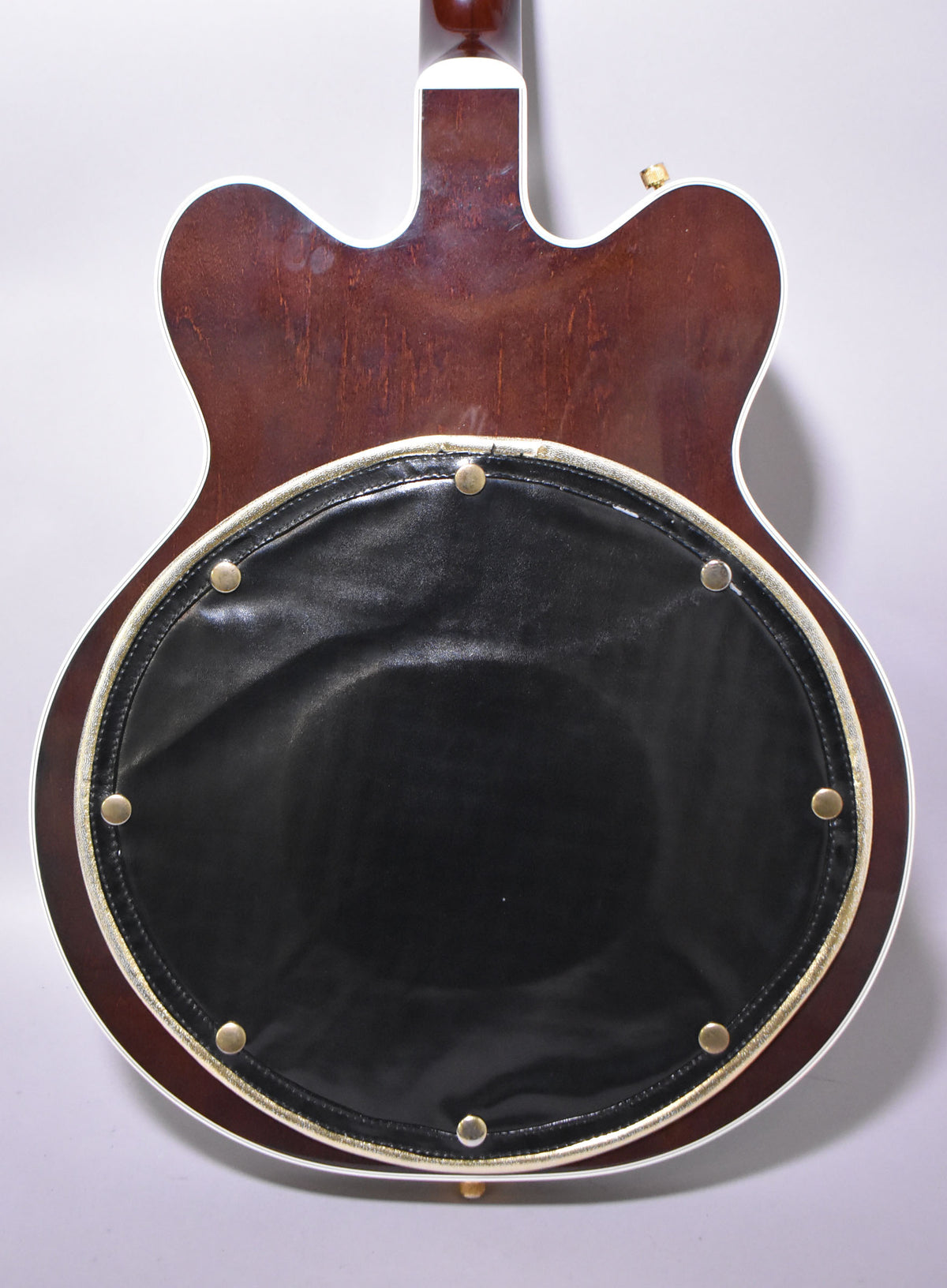 The guitar's dark walnut back is visible from the neck joint down, with a black leather pad secured by brass studs.
