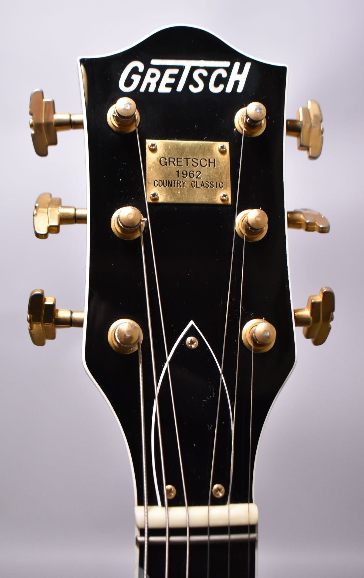 Close-up of the black headstock with gold tuners, a brass plaque, and a white nut, showing some wear on the tuner buttons.