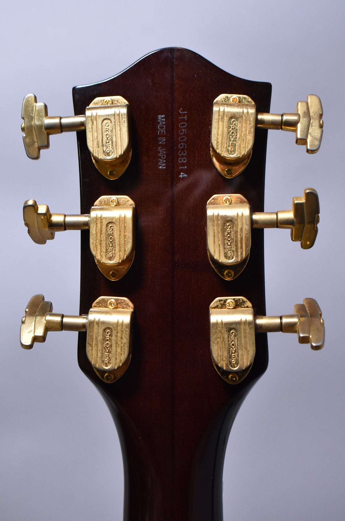 Rear view of the dark walnut headstock, showing six gold Grover tuners with light wear and a serial number.