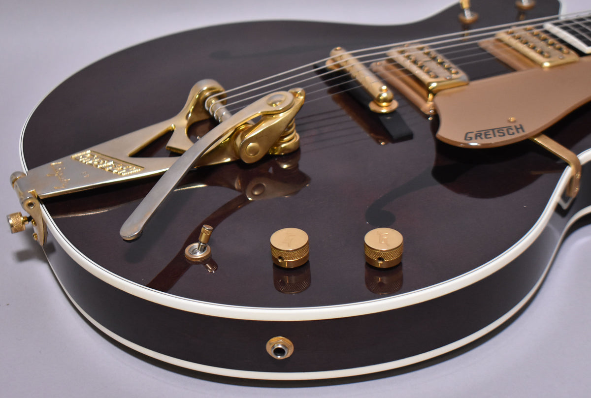 Upper bout of a dark walnut hollowbody guitar with gold Bigsby tremolo, pickups, pickguard, and two knurled control knobs.