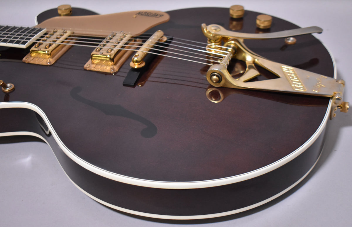 Dark walnut hollow-body guitar, angled from the lower bout, showing gold hardware, Bigsby vibrato, and f-hole.