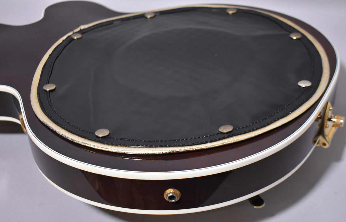 Close-up of the guitar's lower bout, showing the dark brown finish, white binding, and a black padded back with brass studs.