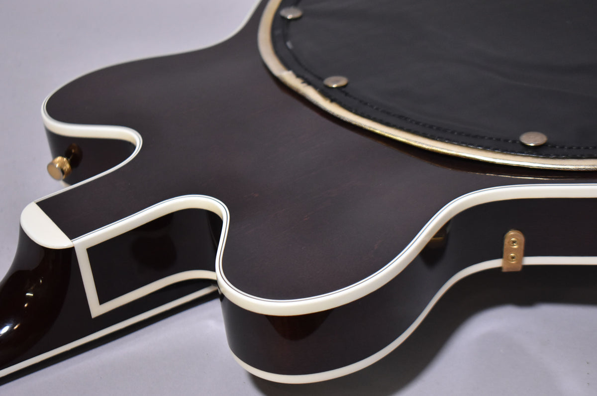 Close-up of the dark walnut guitar body, showing white binding, a gold strap button, and a black armrest with silver studs.