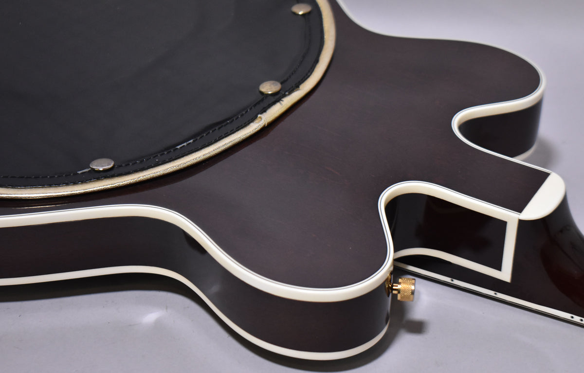Close-up of the dark walnut body, showing the black armrest with brass studs and some wear on the binding.