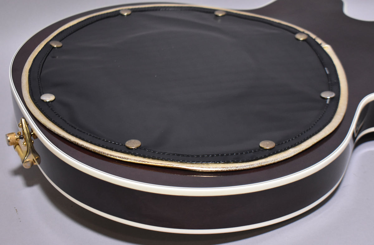 Close-up of the guitar's dark brown back, showing a large black circular pad with gold trim and eight brass snaps.