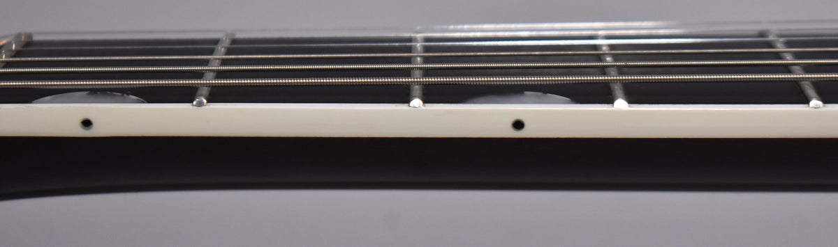Close-up of the guitar's dark fretboard and strings, showing cream binding with black side dot markers and white pearloid block inlays.