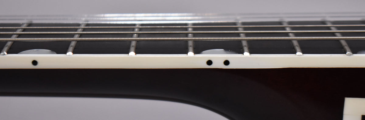 Close-up of the fretboard's side, showing the cream binding, dark side dots, and a few frets with minor wear.