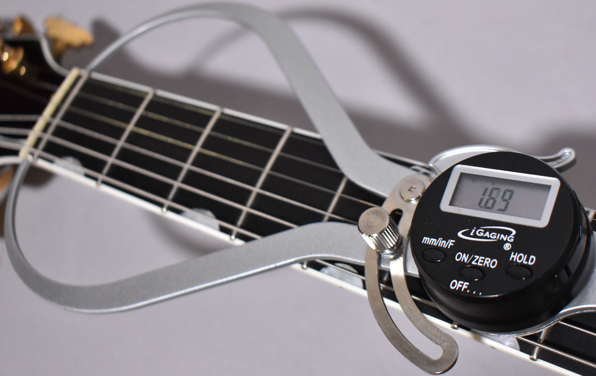 A digital caliper measures the nut width of the dark walnut neck, showing 1.69 inches on the display.