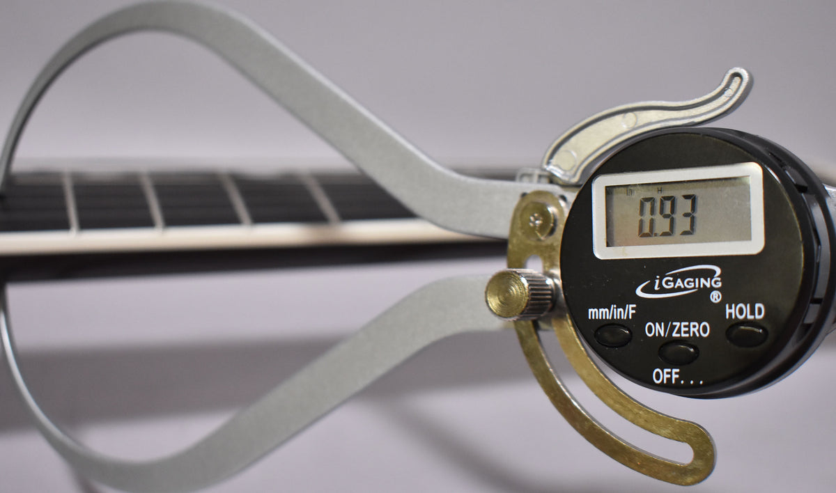A digital caliper measures the fret height on the guitar's dark fretboard, displaying "0.93" on its screen.