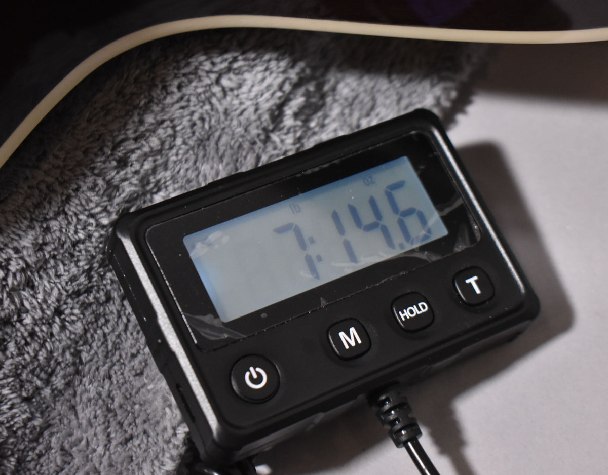 Digital scale displaying 7 lbs 14.6 oz, with power, mode, hold, and tare buttons, resting on a grey fuzzy surface.