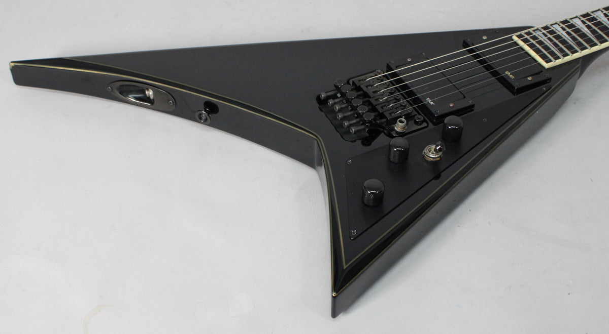 The black V-shaped guitar body, with gold pinstripes, is angled from the input jack to the black Floyd Rose bridge and controls.
