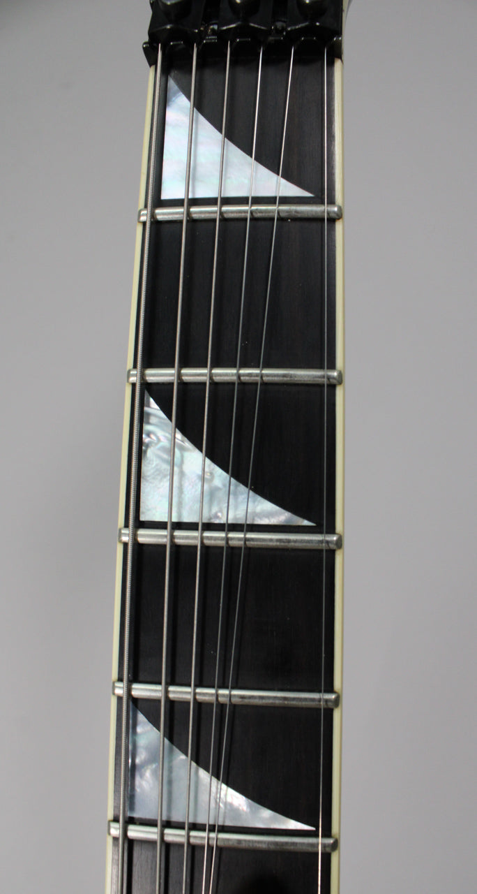 Close-up of the black fretboard with pearloid sharkfin inlays, showing the first five frets and a cream binding along the edge.