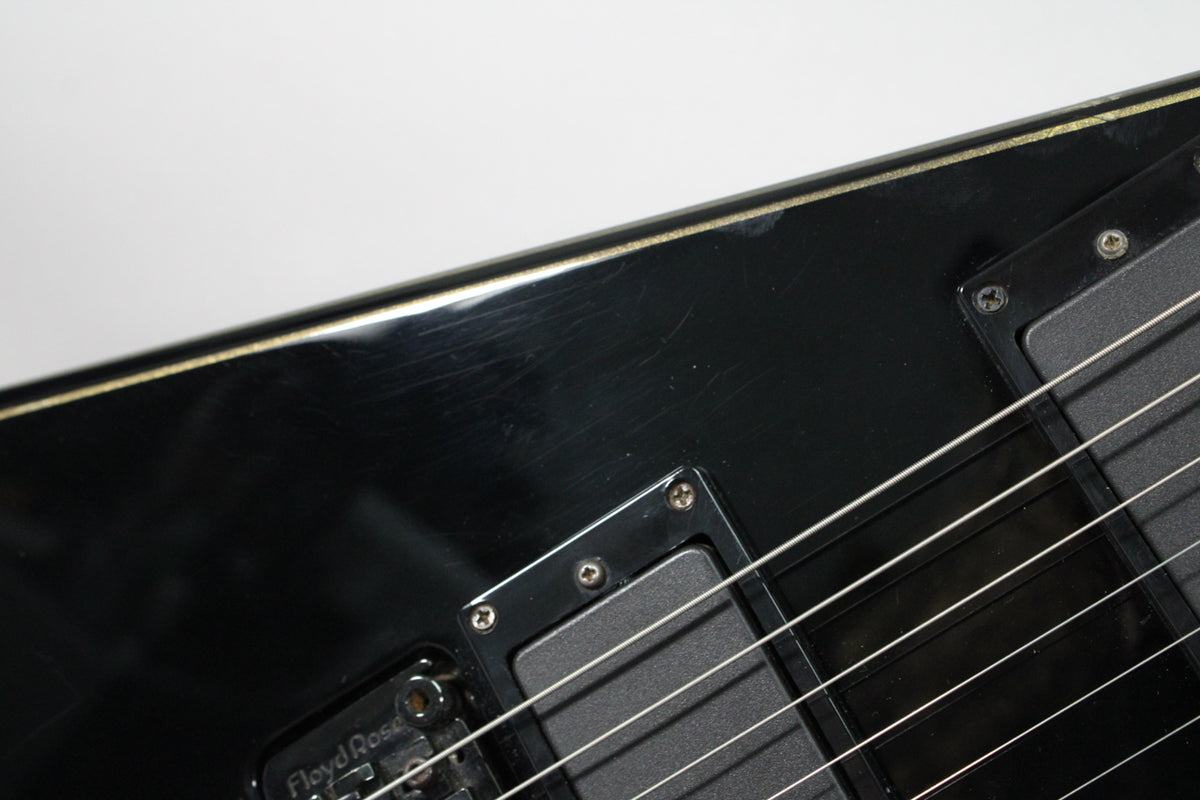 A close-up of the guitar's black body, showing light scratches, gold pinstriping, and a black humbucker pickup with a Floyd Rose tremolo.