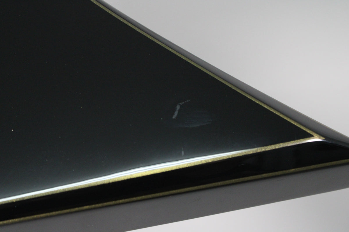 Close-up of the guitar's black body with gold pinstriping, showing a small white scuff mark and a faint scratch on the glossy finish.