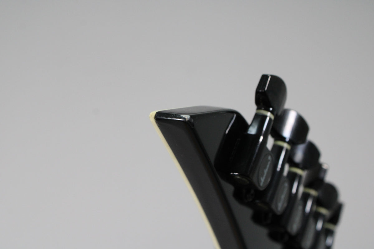 Close-up of the black headstock's pointy end, showing a small chip on the top edge and four black tuning pegs in a row.