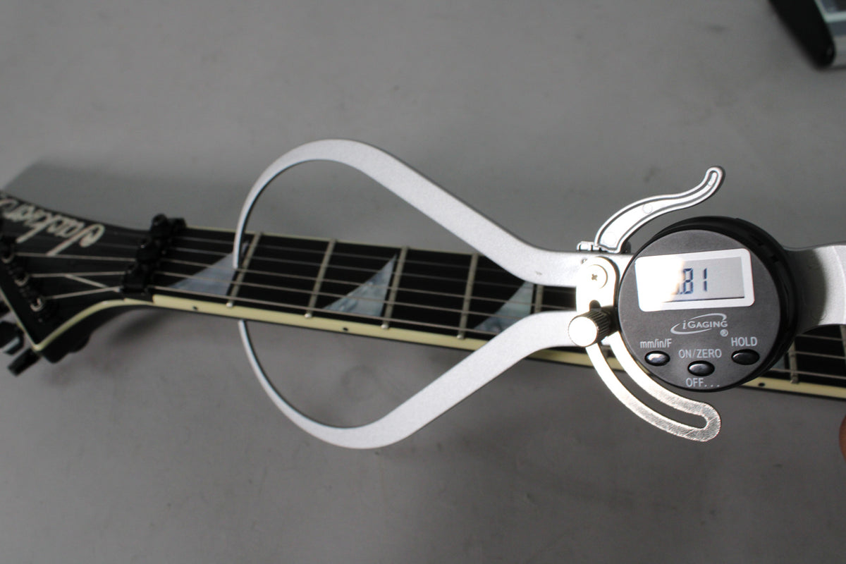 A digital caliper measures the black fretboard with pearloid sharkfin inlays, showing a reading of .81.