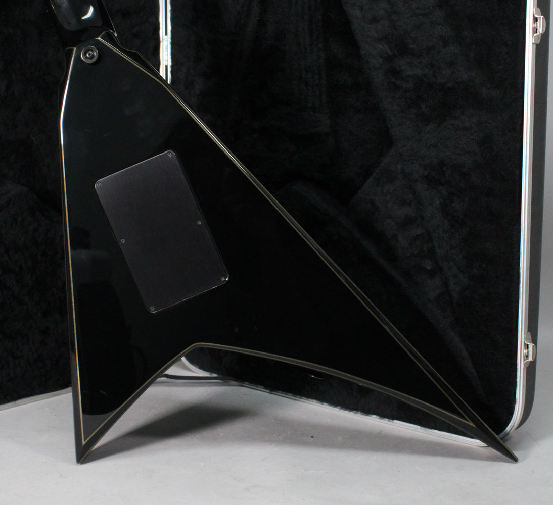 The back of a glossy black V-shaped guitar with gold pinstripes, showing a rectangular control cavity cover and some light wear.