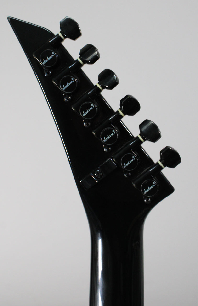 The black guitar headstock, angled left, features six black tuners with white string posts and a black locking nut.