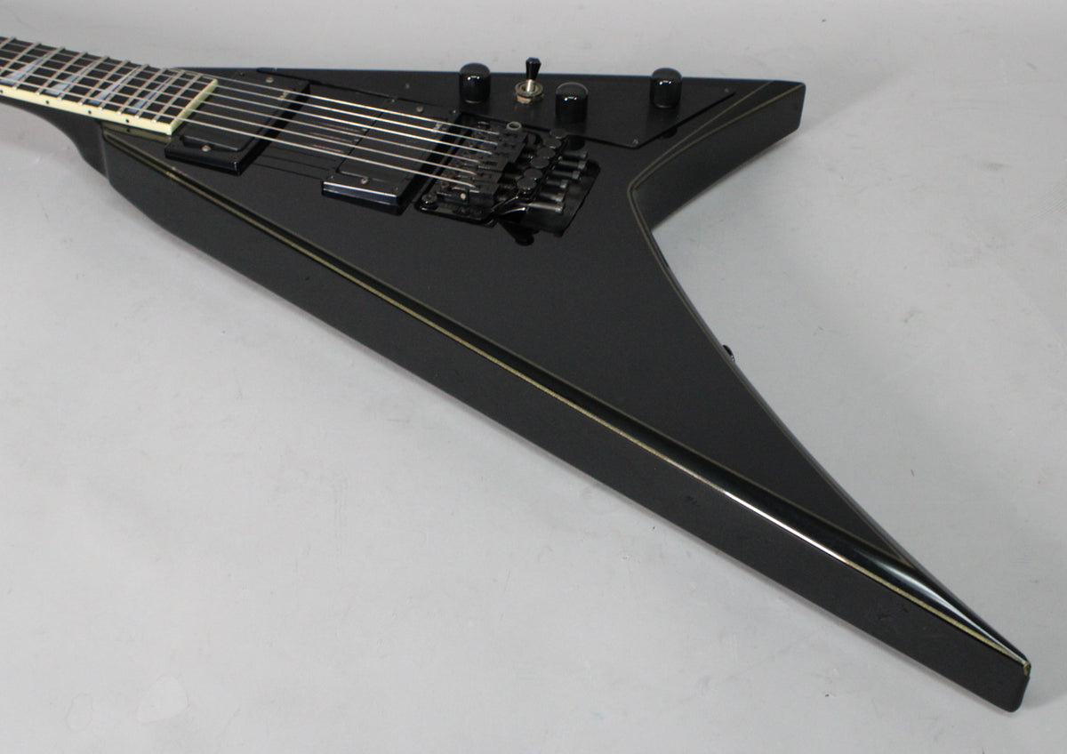 The black V-shaped guitar body, with gold pinstripes, is angled from the neck to the pointed lower wing, showing black hardware.