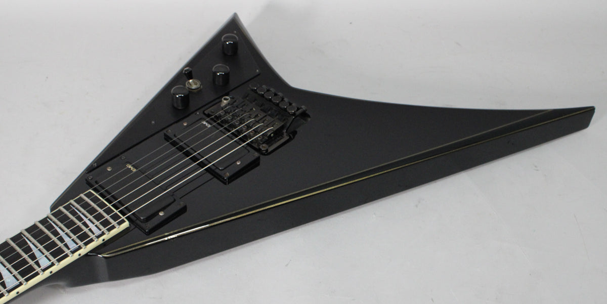 Overhead view of the black V-shaped guitar body, showing the black humbucker pickups, black Floyd Rose tremolo, and gold pinstripe.