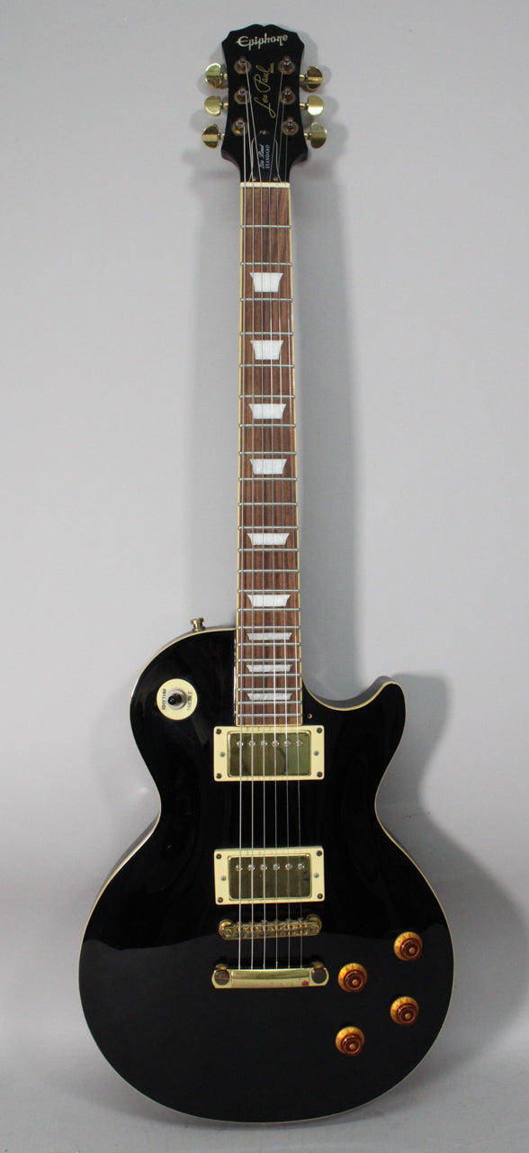 Full-length, glossy black electric guitar with gold hardware, cream binding, trapezoid inlays, and amber control knobs.