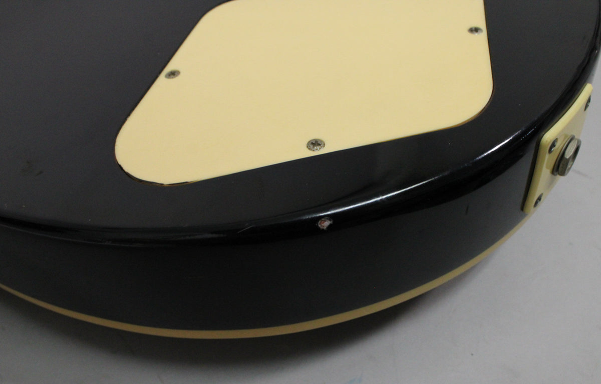 Close-up of the guitar's lower bout, showing the black finish, cream binding, and a chip near the cream output jack plate.