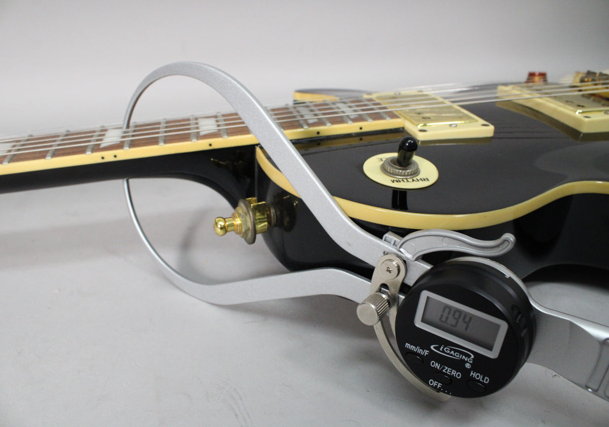 Close-up of the guitar's glossy black body and neck, with a digital caliper measuring the neck thickness at 0.94 inches.