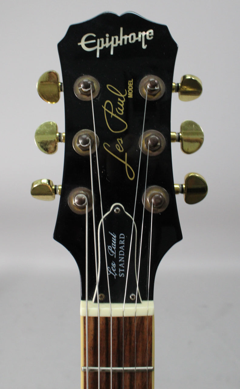 Close-up of the black headstock with gold tuners, showing light wear and a cream nut above the dark fretboard.