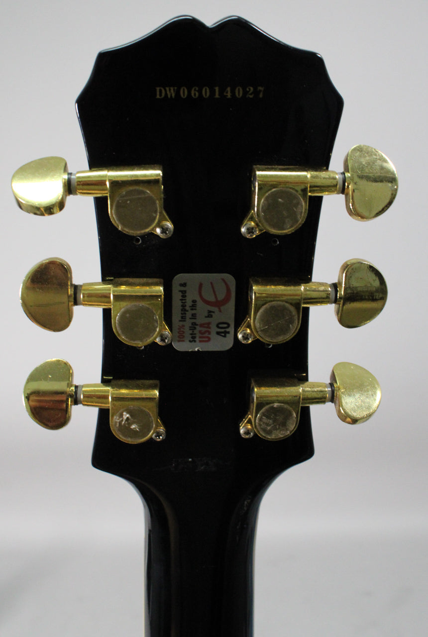 Rear view of the black headstock and neck, showing six gold tuners with some wear and a "USA by 40" sticker.