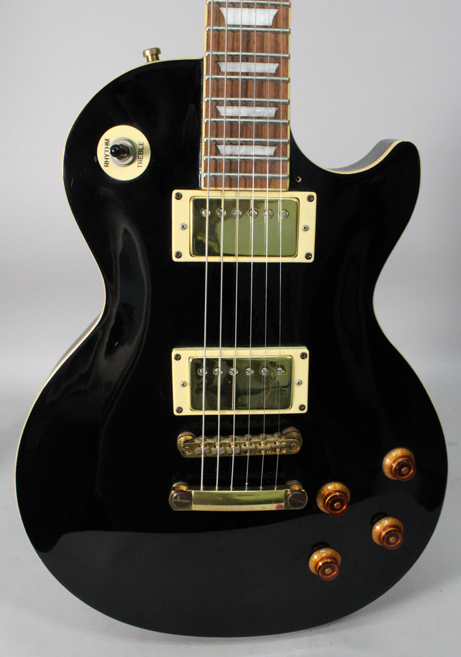 The glossy black guitar body, with cream binding, features gold hardware, two cream-framed humbuckers, and four amber control knobs.