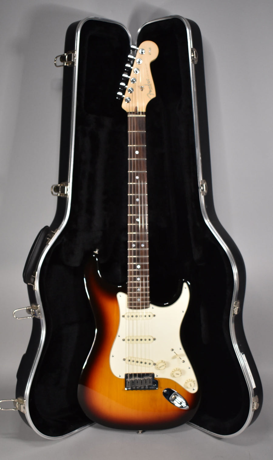 Full-length view of a sunburst Stratocaster with a white pickguard, three single-coil pickups, and a tremolo bridge, resting in its open hard case.