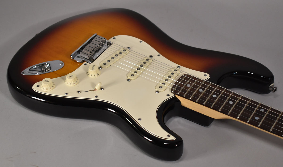 Sunburst Stratocaster, angled from above, showing the body, white pickguard, three single-coil pickups, and part of the fretboard.