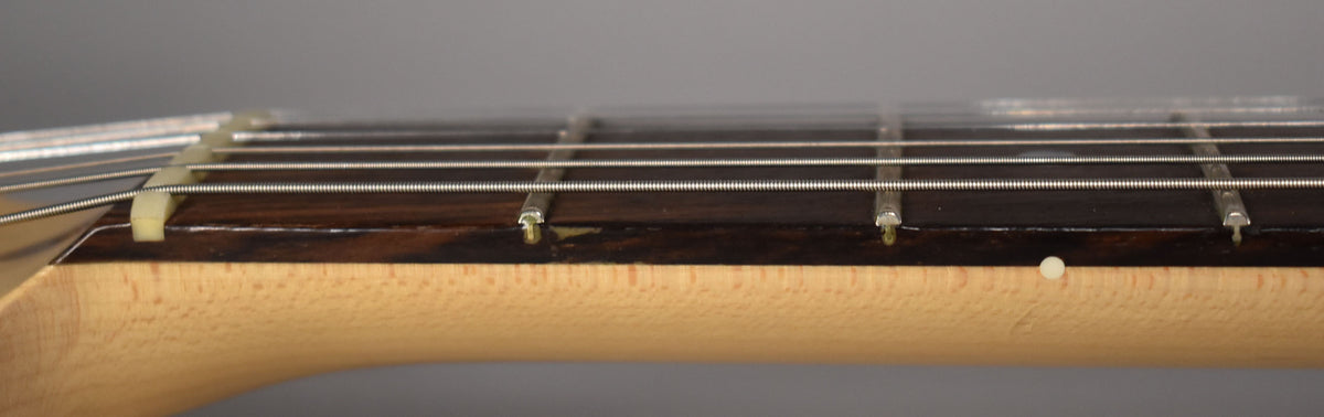 Close-up of the guitar's maple neck and dark fretboard, showing the nut, frets, strings, and a single white side dot marker.