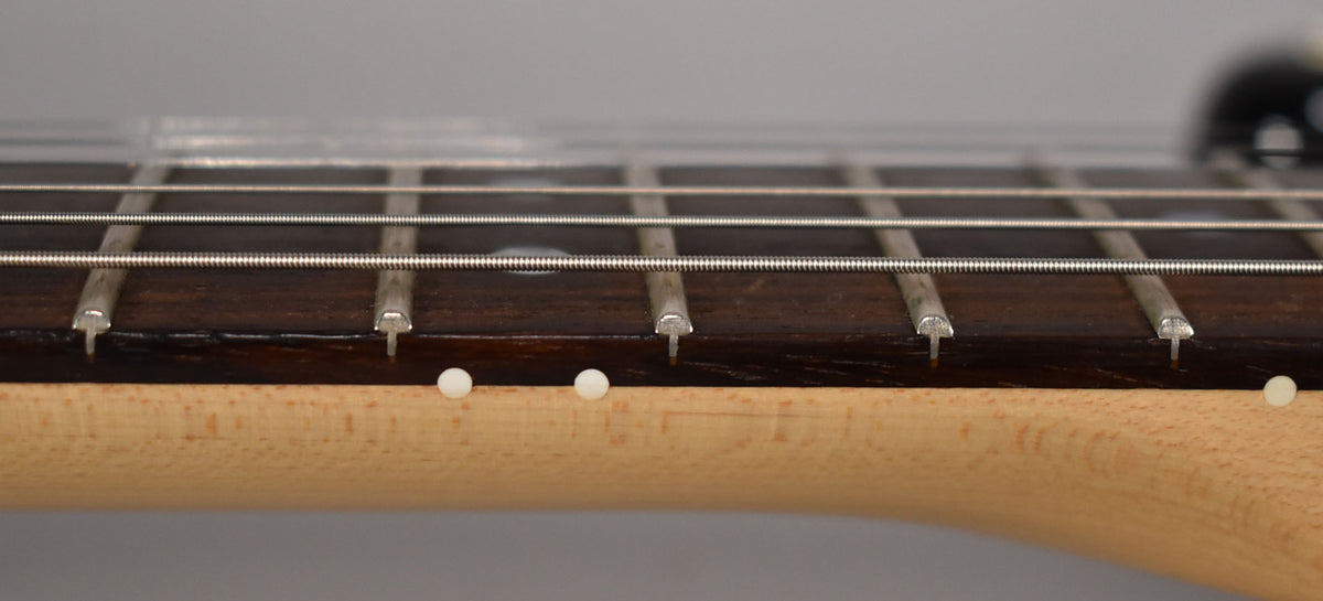 Close-up of the dark rosewood fretboard and light maple neck, showing frets, strings, and three white side dot markers.
