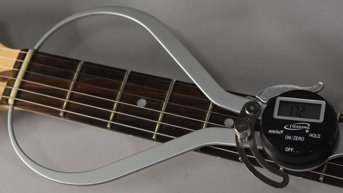 A digital fret rocker measures the dark rosewood fretboard with light fret markers and frets, showing "1.72" on its screen.