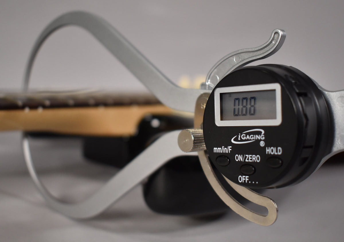 A digital caliper measures the neck relief of the sunburst Stratocaster, displaying "0.00" on its screen.