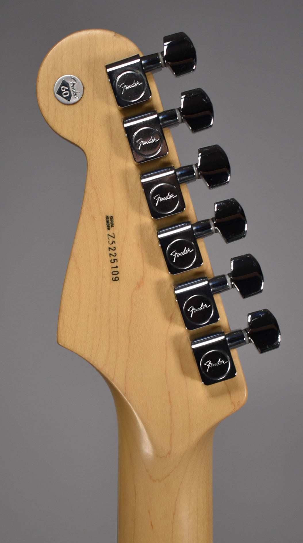 The back of a light maple headstock and neck, showing six chrome tuners and a "60" anniversary button.