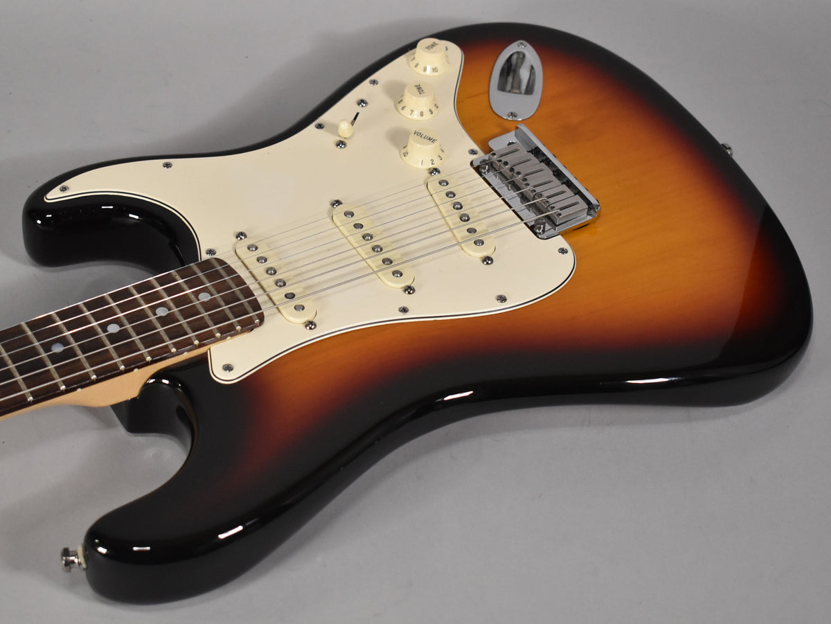 Sunburst Stratocaster body, angled from the neck, showing cream pickguard, three single-coil pickups, and chrome tremolo bridge.