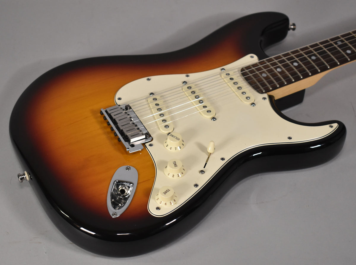 Sunburst Stratocaster body, angled from above, showing the cream pickguard, three single-coil pickups, chrome bridge, and input jack.