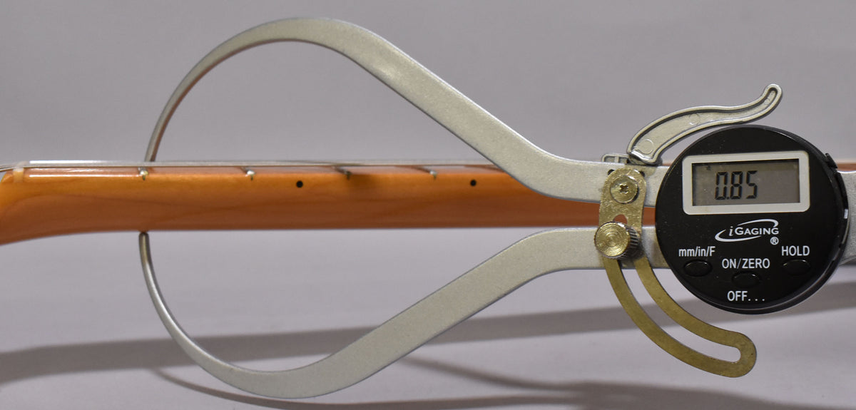 A digital caliper measures the maple neck's thickness at 0.85 inches, showing the fretboard and frets from the side.
