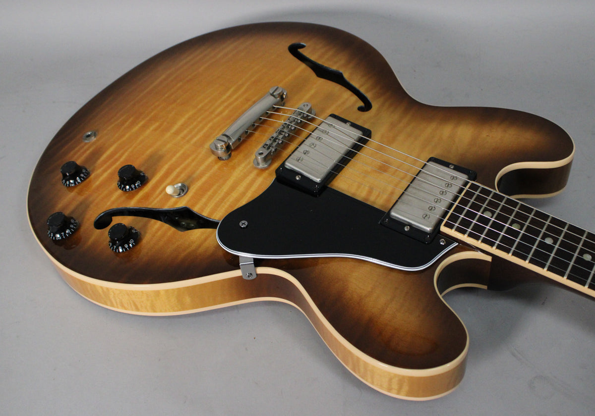 Upper body of a sunburst semi-hollow guitar, showing the figured maple top, f-holes, black pickguard, four black knobs, and two chrome humbuckers.
