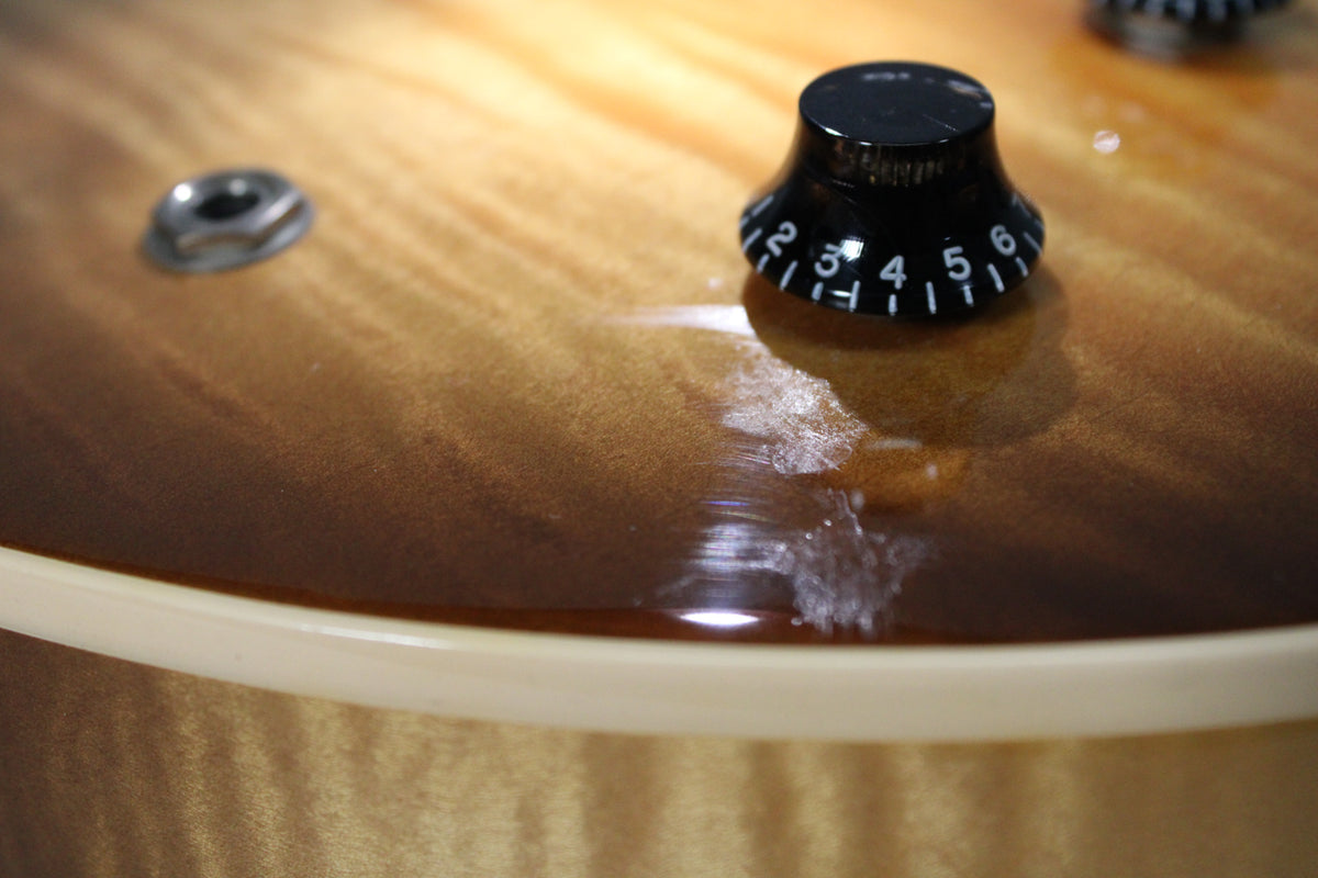 Close-up of the flamed sunburst top with cream binding, a black top-hat control knob and a small metal ring.
