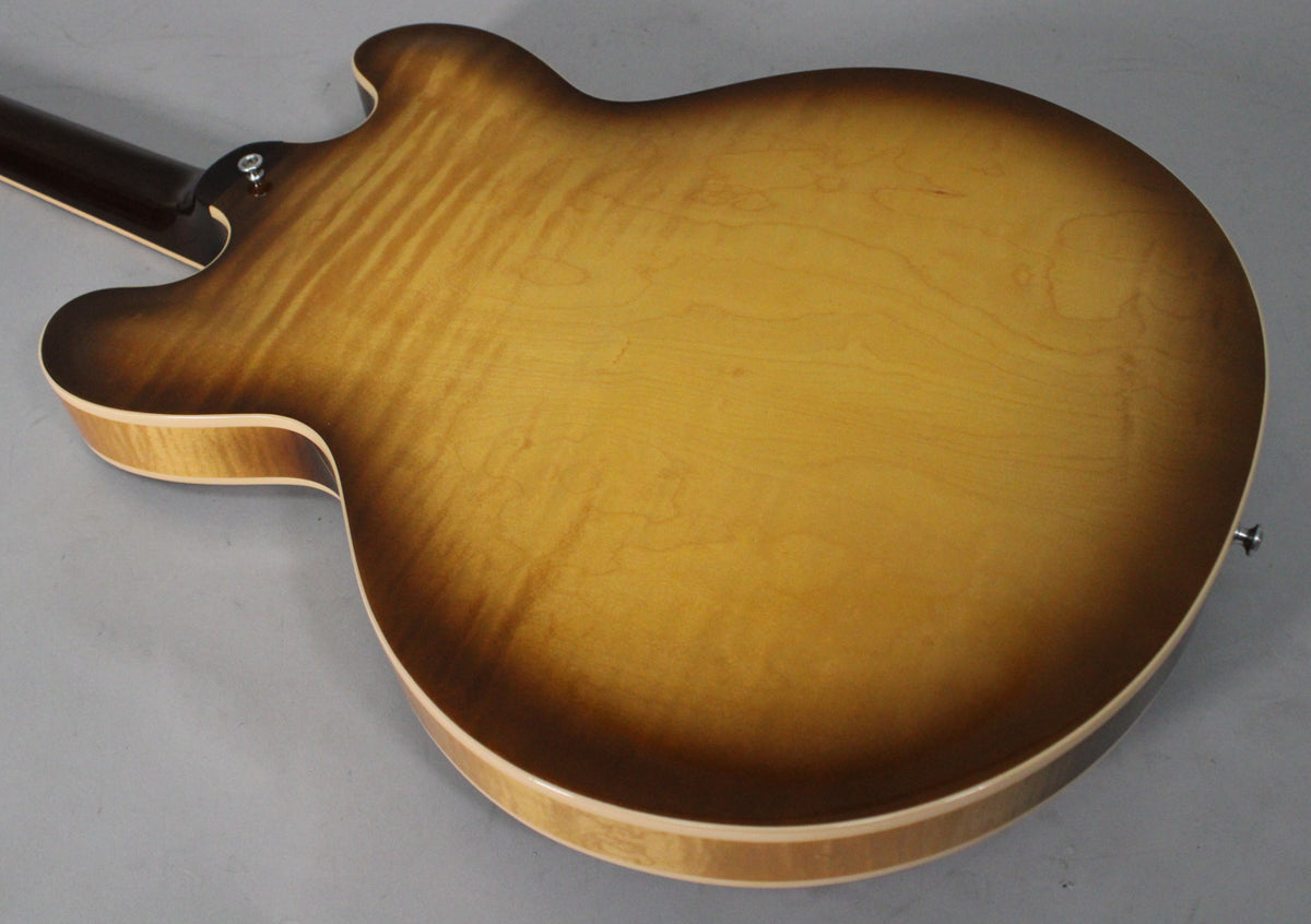 The back of a figured sunburst semi-hollow guitar, showing the flame maple grain and a strap button near the neck heel.