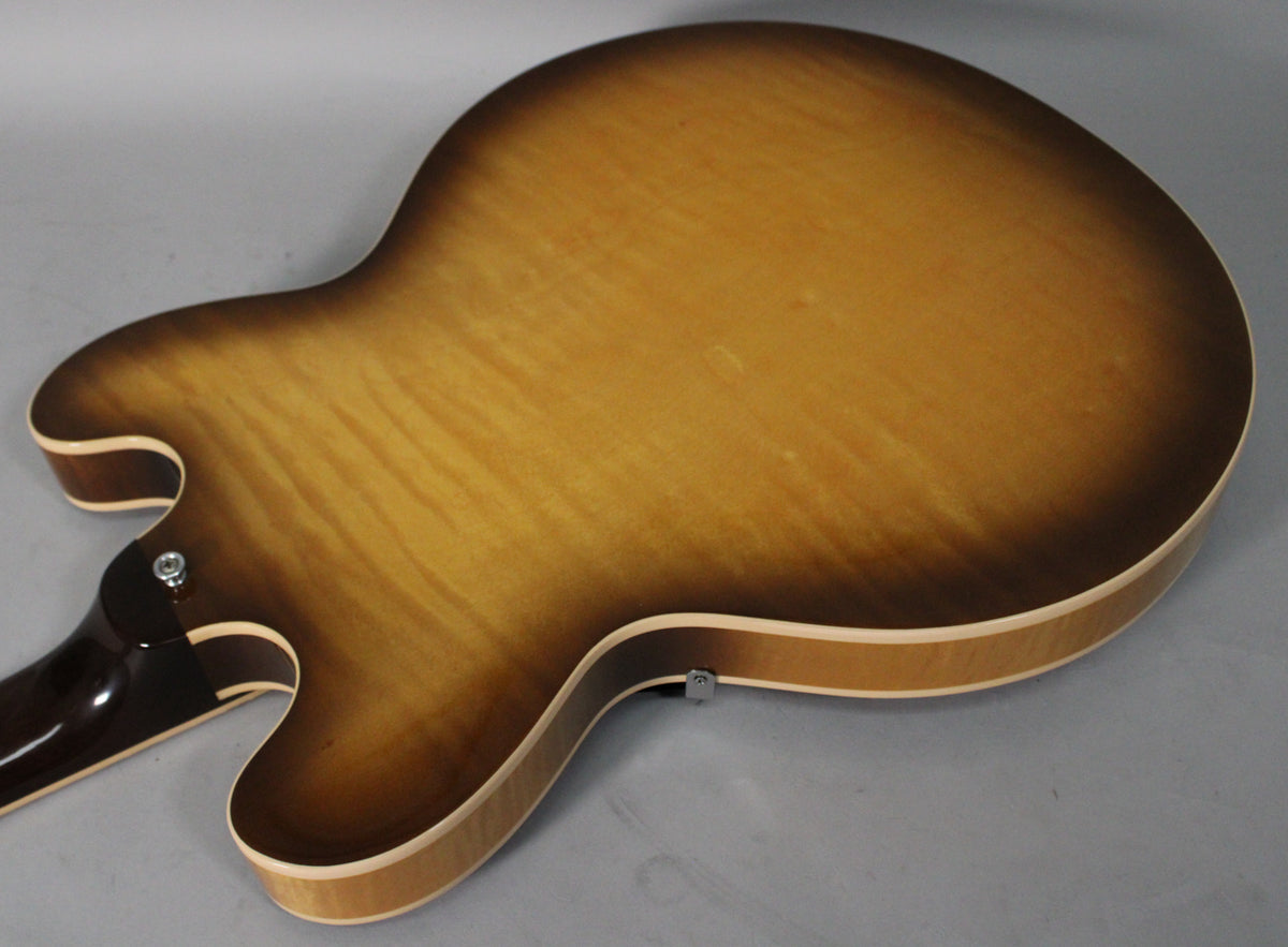 The back of a sunburst semi-hollow guitar, showing the figured maple grain, dark brown neck heel, and a strap button.