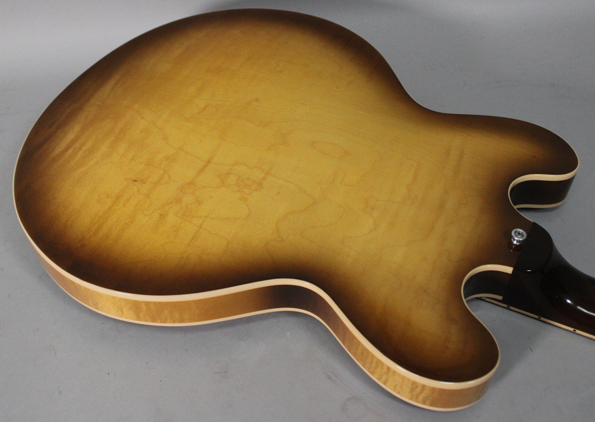 The guitar's figured sunburst back, showing light flame maple, with a strap button visible at the heel.